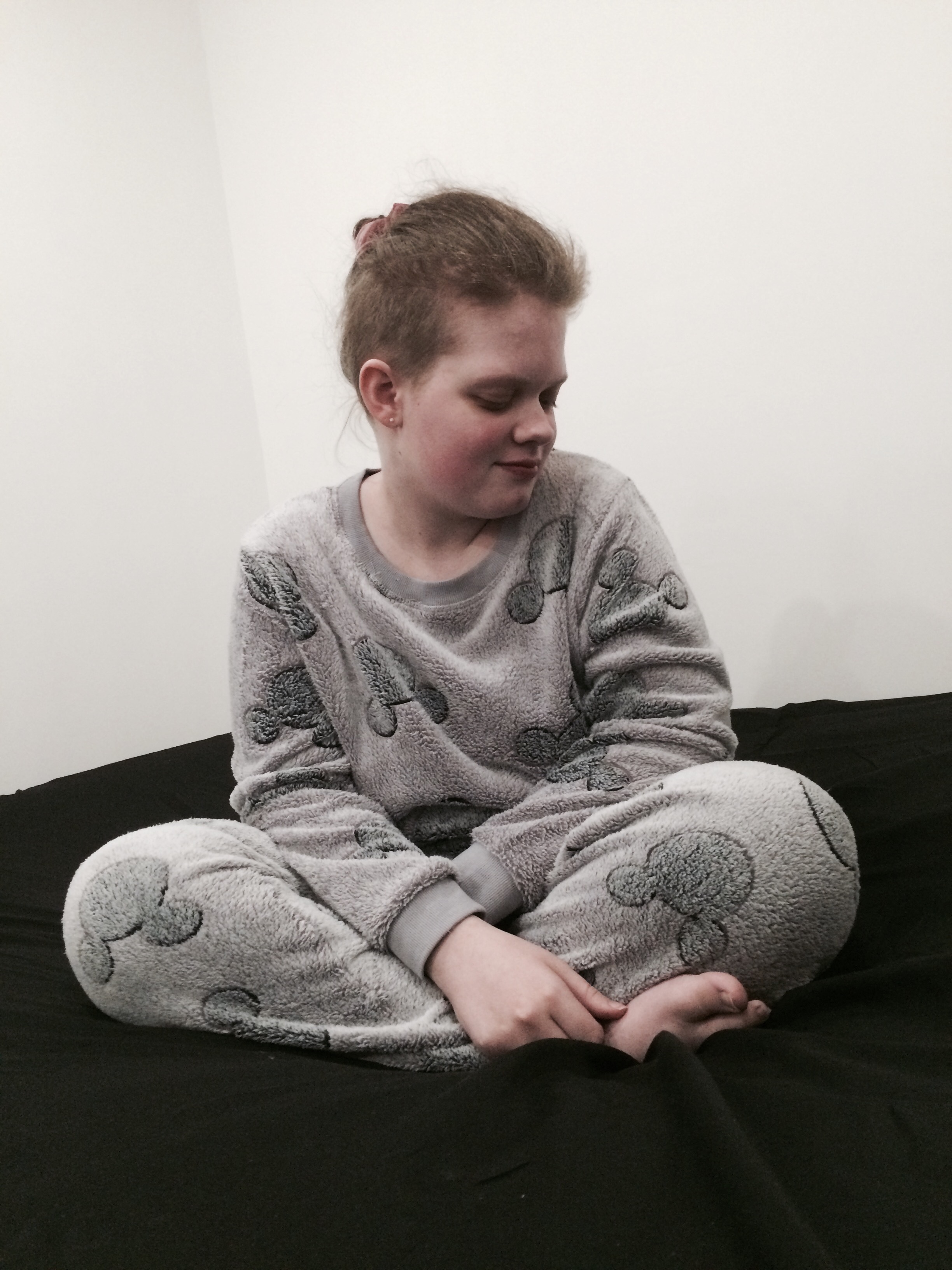 Tiegan Elise sat on a bed, wearing fleecy grey pyjamas which have silhouettes of Mickey Mouse’s head