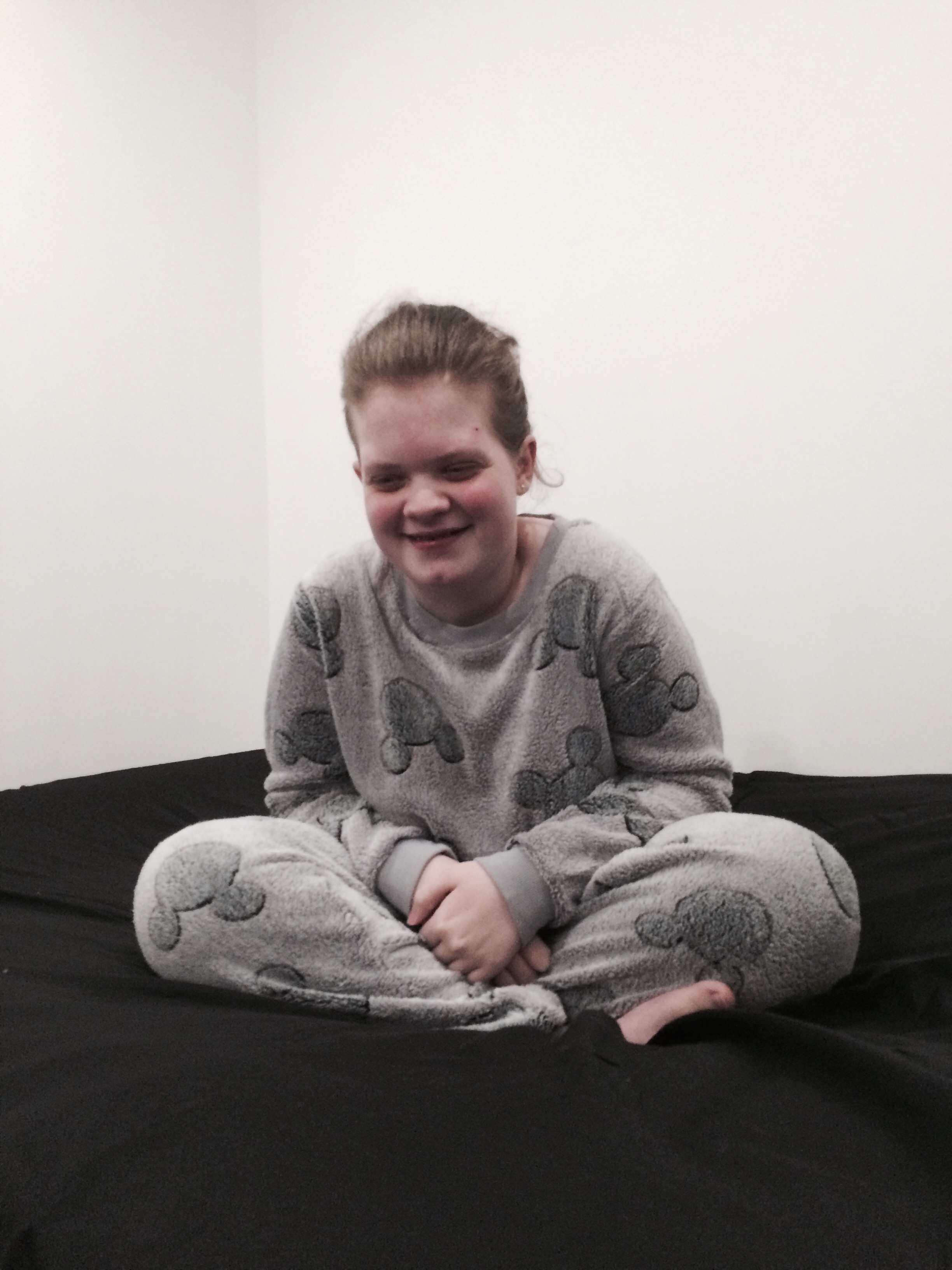 Tiegan Elise sat on a bed, wearing fleecy grey pyjamas which have silhouettes of Mickey Mouse’s head