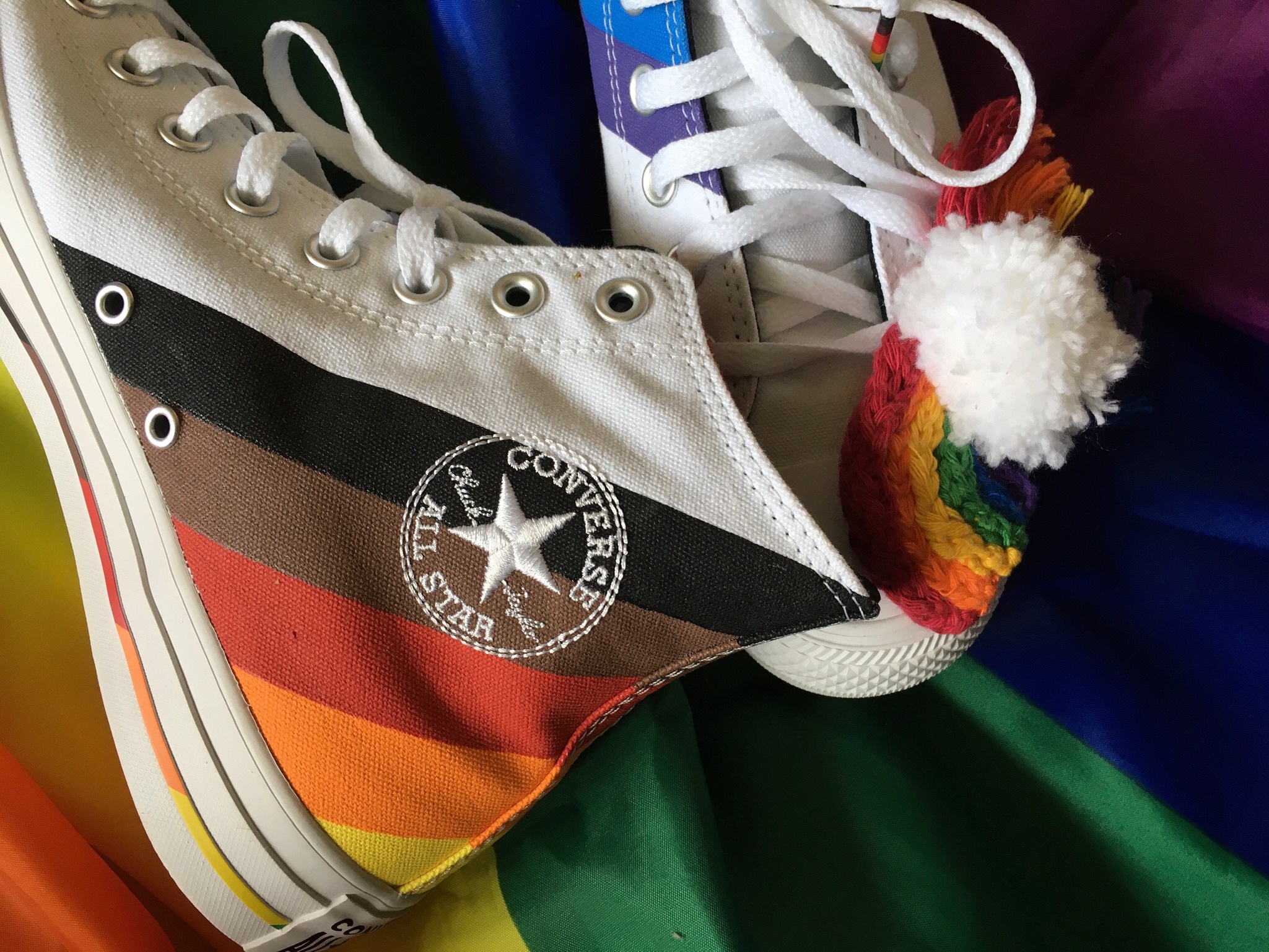 A crafted pride rainbow sits on a pair of pride converses which are on a large pride flag.