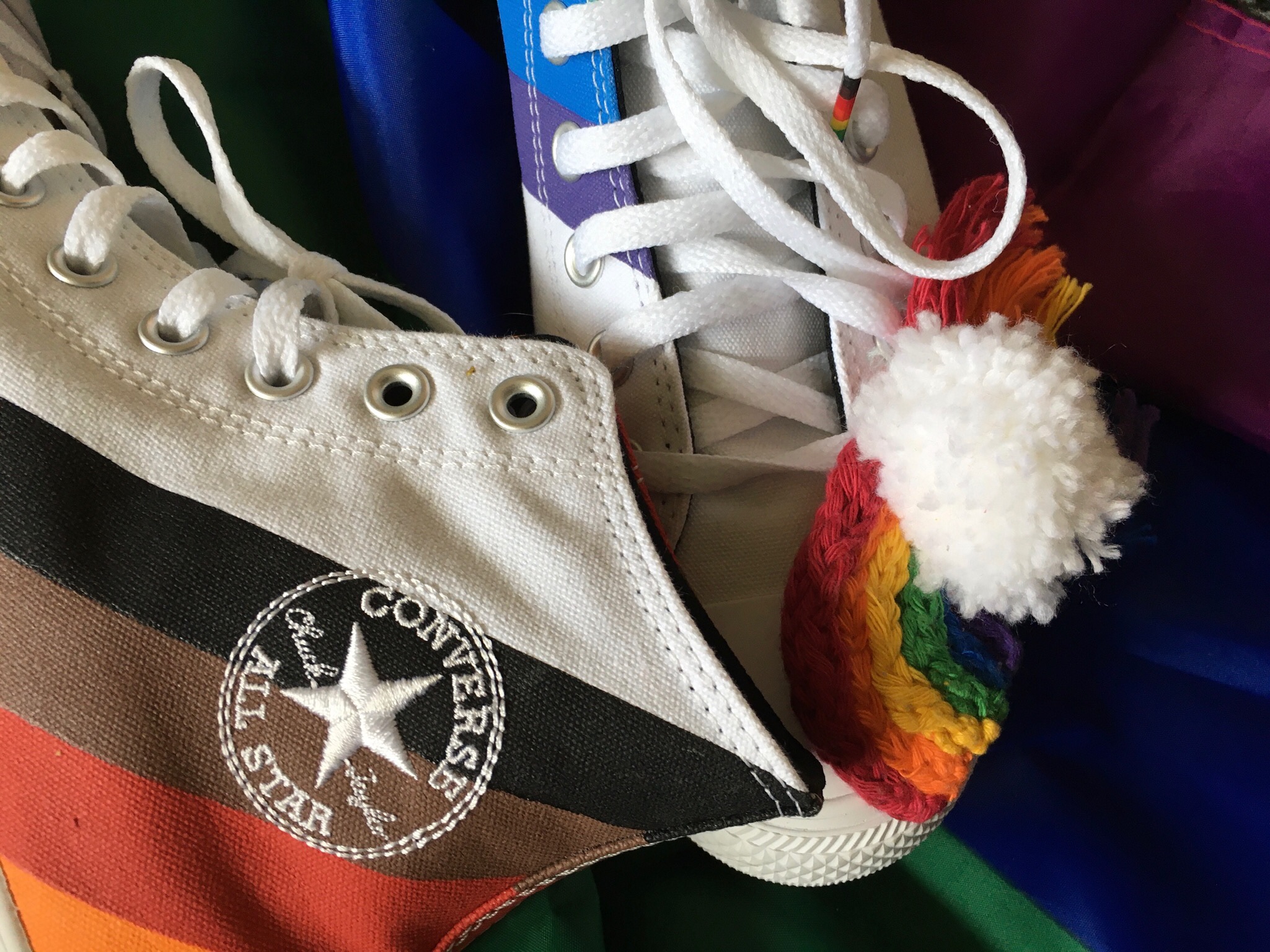 A crafted pride rainbow sits on a pair of pride converses which are on a large pride flag.