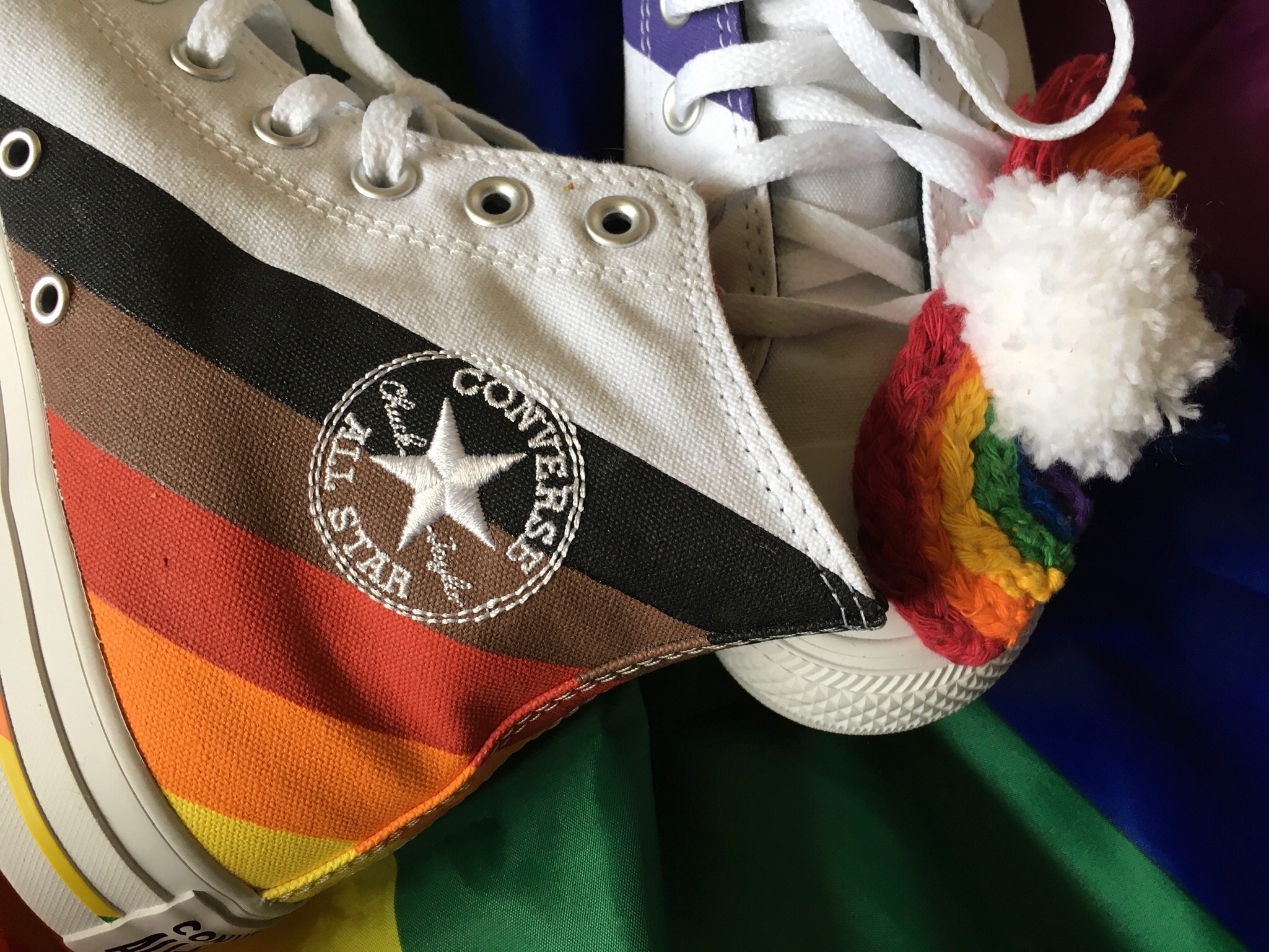 A crafted pride rainbow sits on a pair of pride converses which are on a large pride flag.