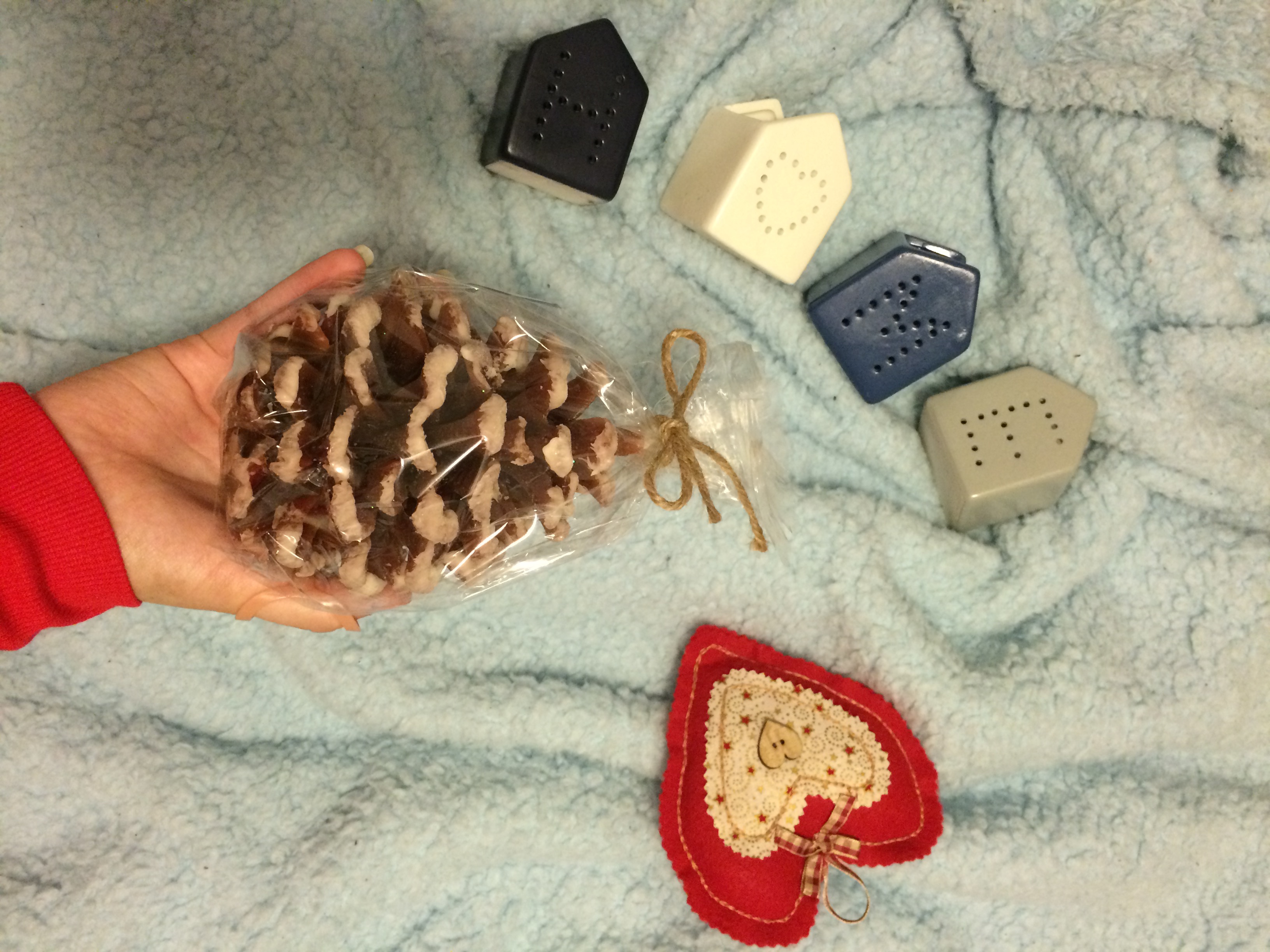 A hand holds a pinecone candle over a fluffy blue blanket which candles making up the word “home” and a felt heart lay on.