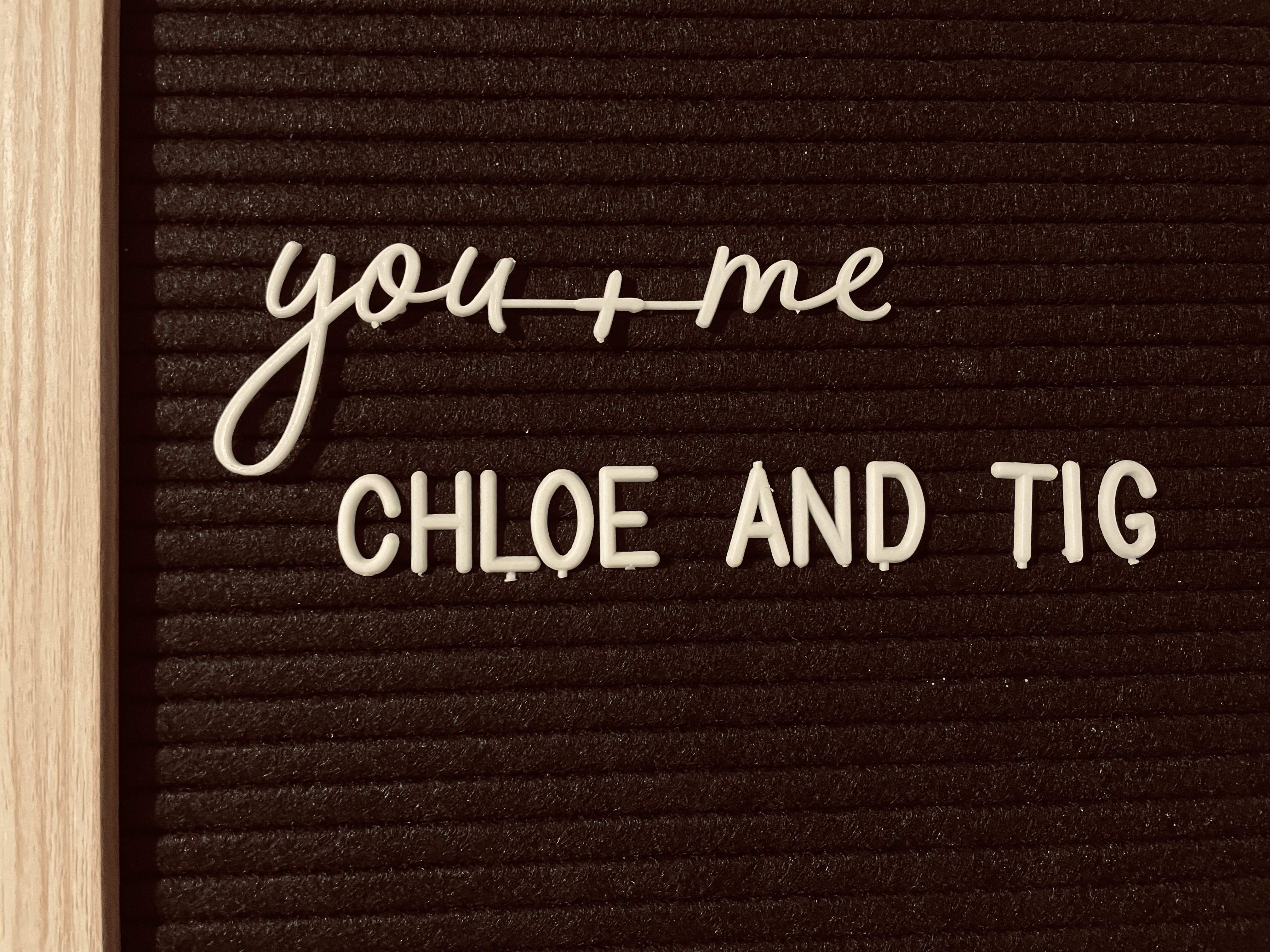 “you + me” in continuous script above “Chloe And Tig” on a letter-board.