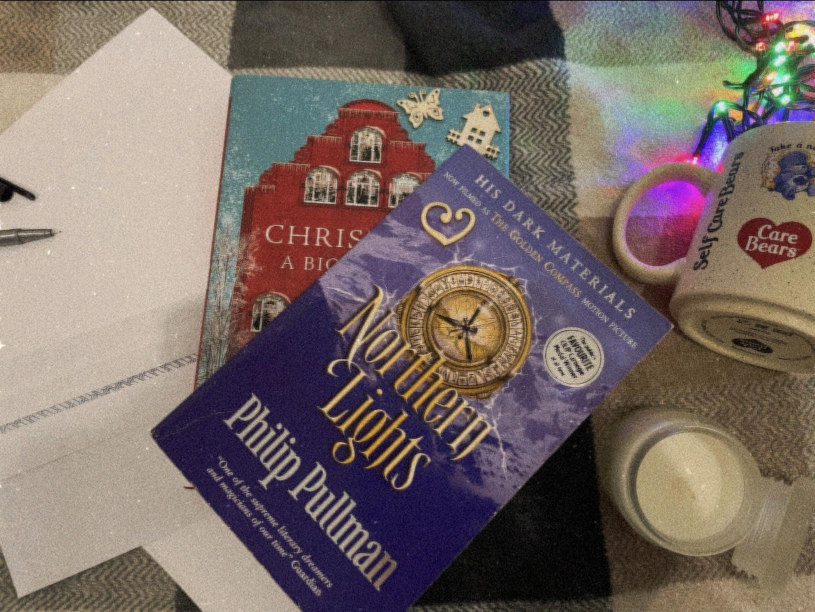 Fairy lights in a mug, letter writing material, a candle, a Christmas book and Philip Pullman’s “Northern Lights” on a tartan throw