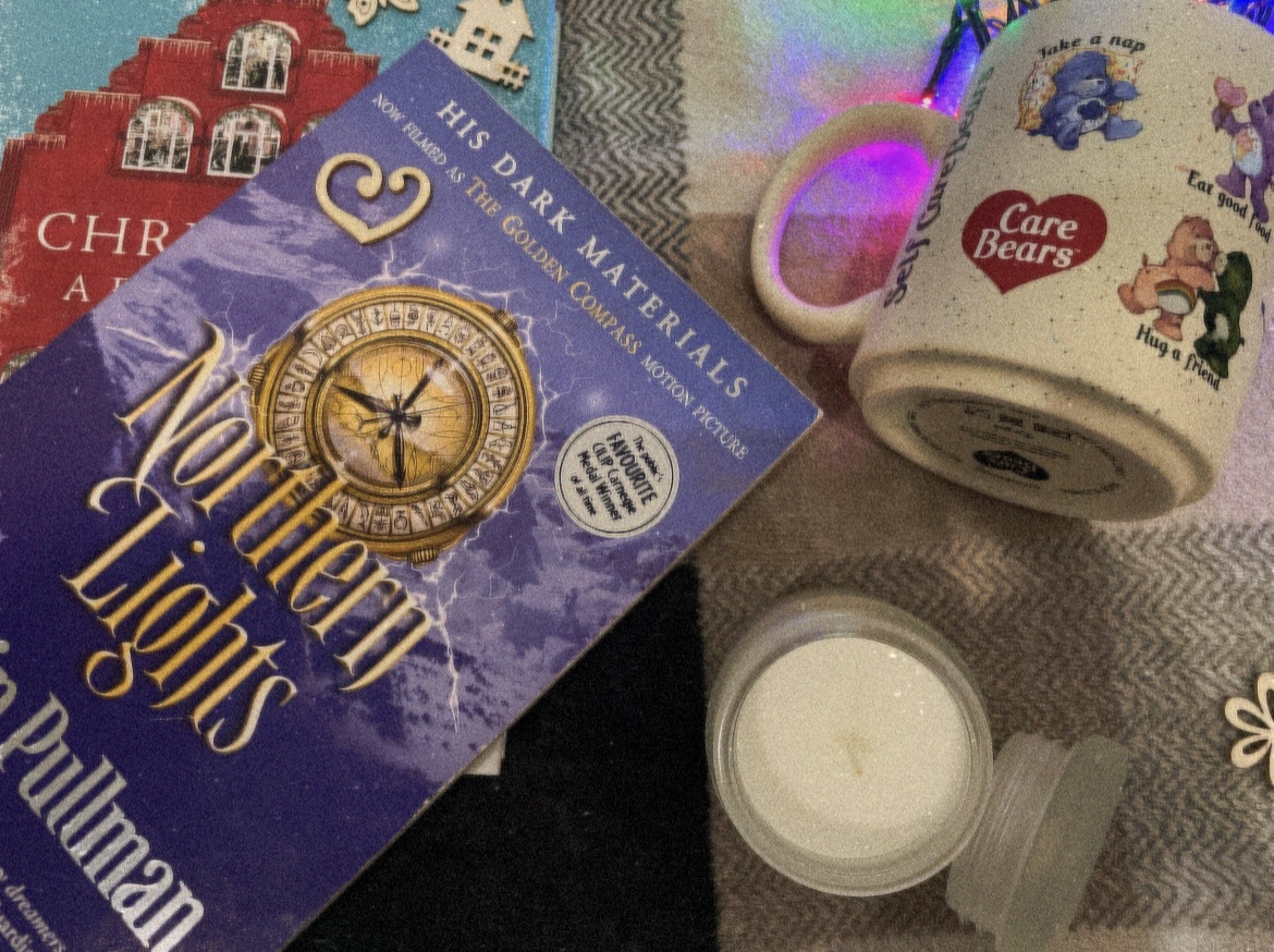 Fairy lights in a mug, letter writing material, a candle, a Christmas book and Philip Pullman’s “Northern Lights” on a tartan throw
