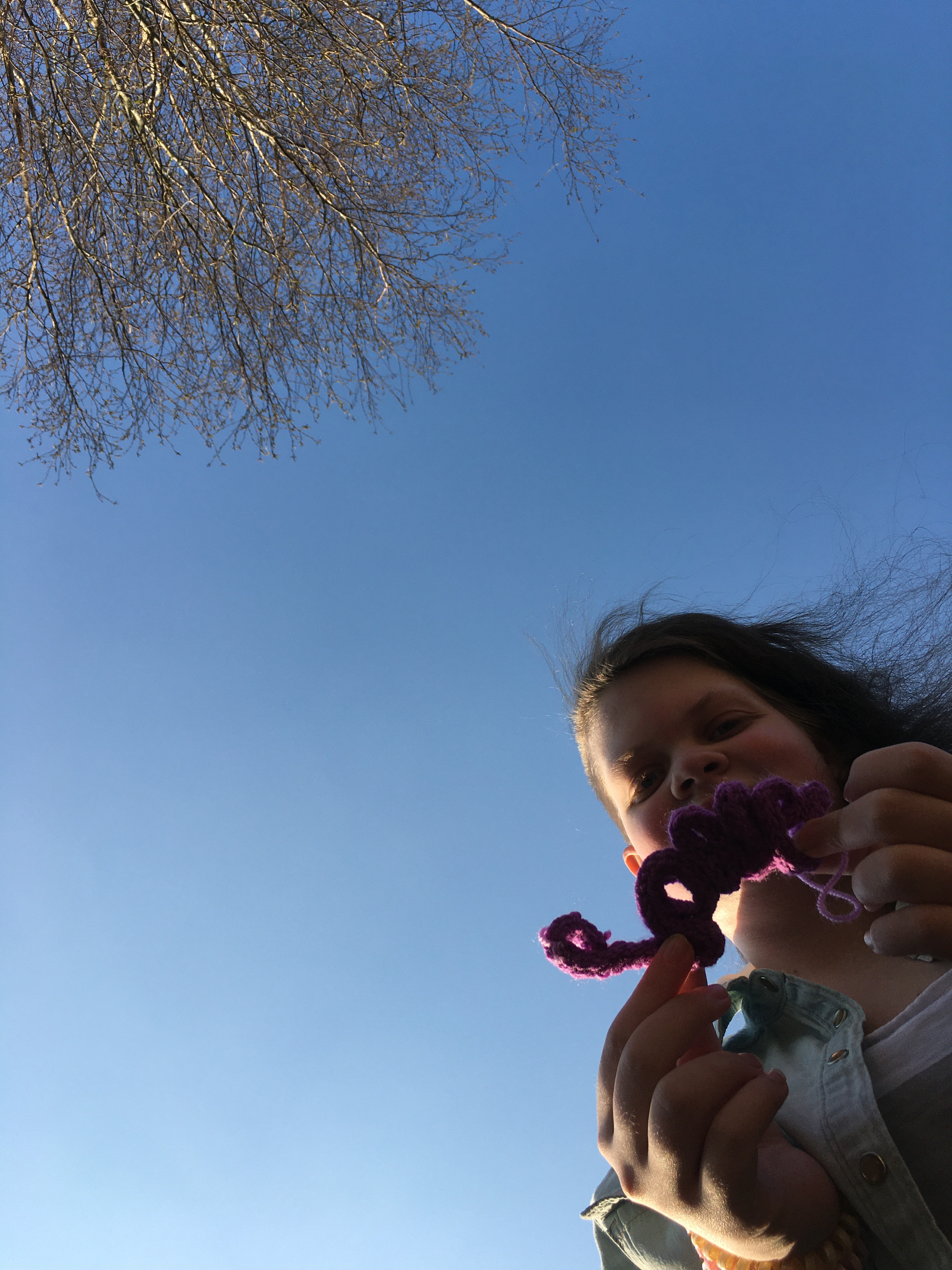 Tig holding a french knitted “Love” shaped sign under a blue sky.