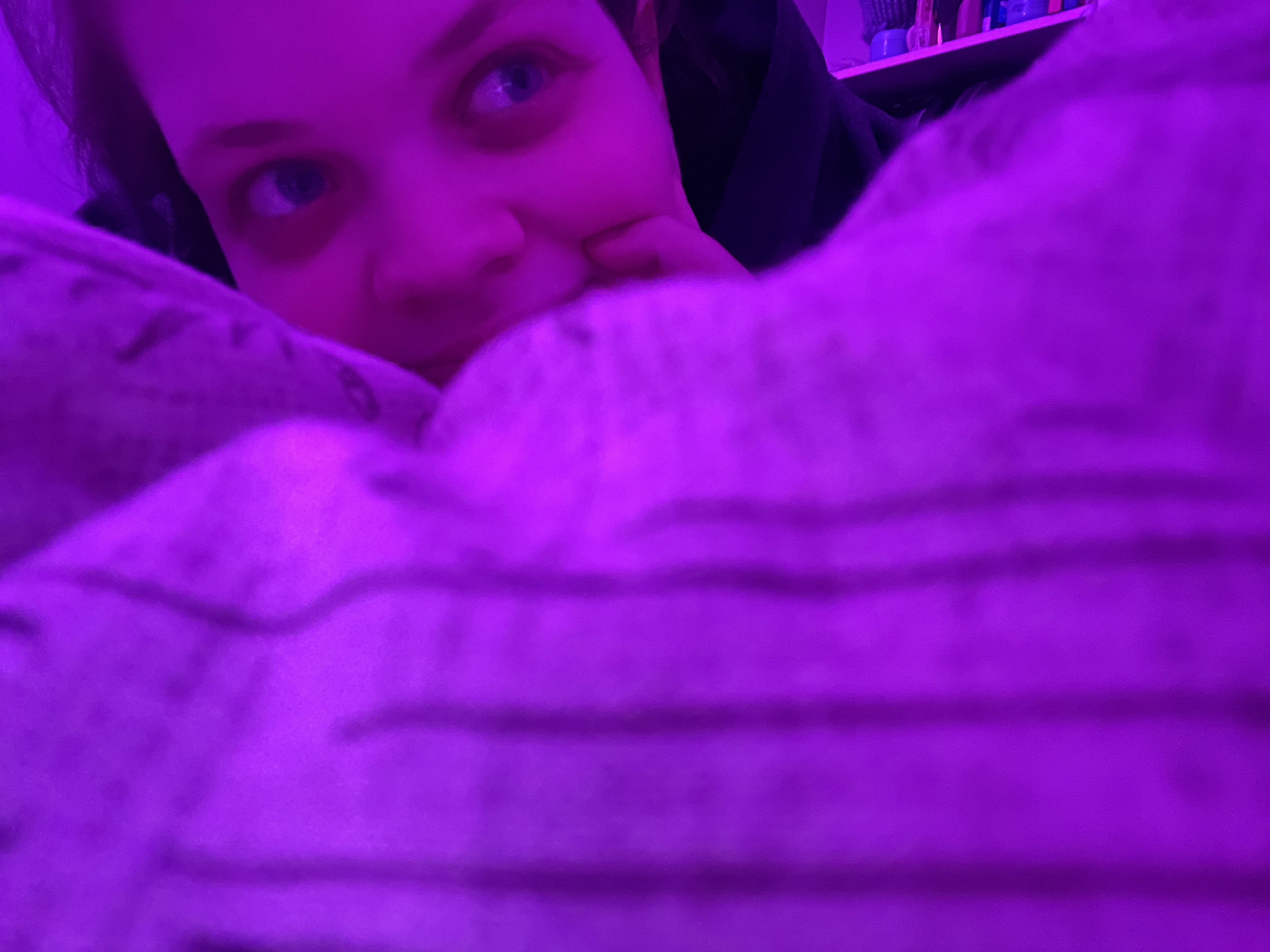 Tig lays belly-first, sinking into a duvet. They look to the top right; one hand under their chin.