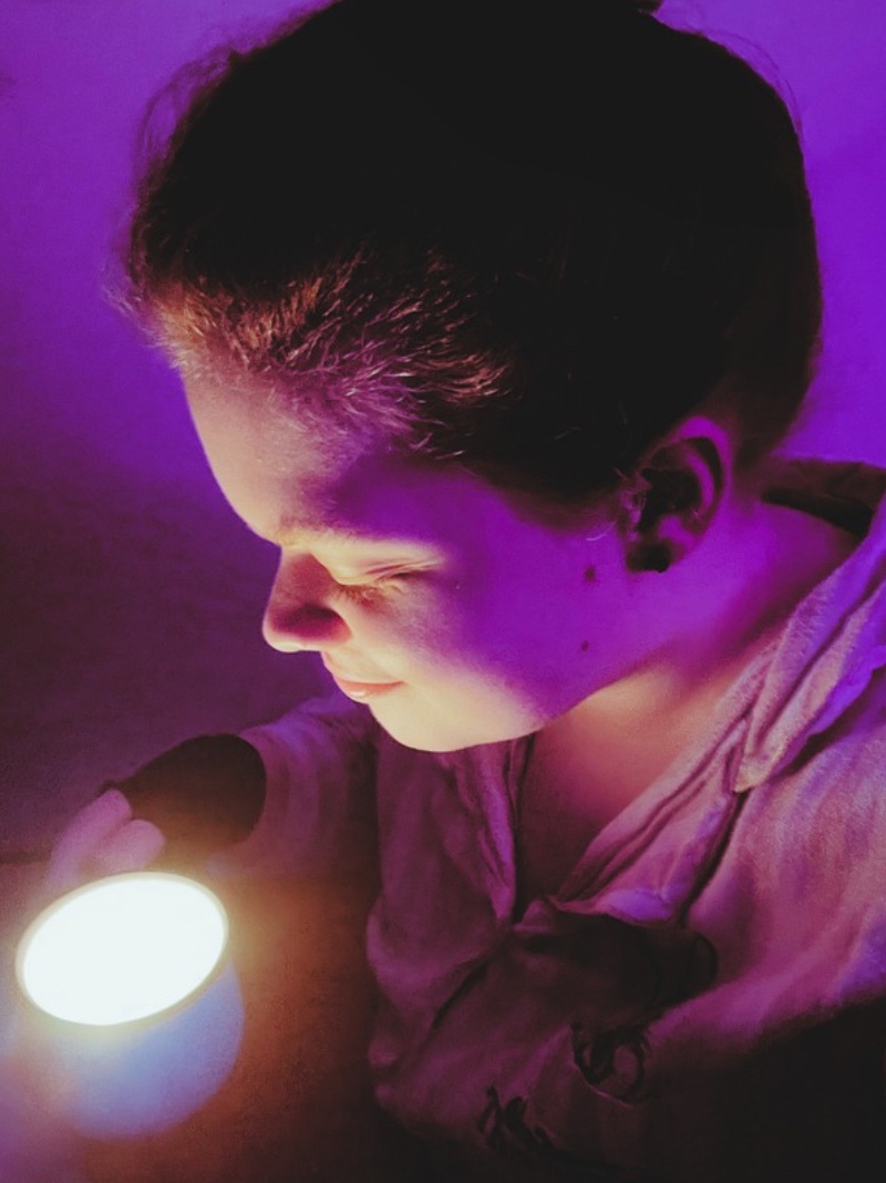 Tig holds a mug candle that they look down at with a small smile 