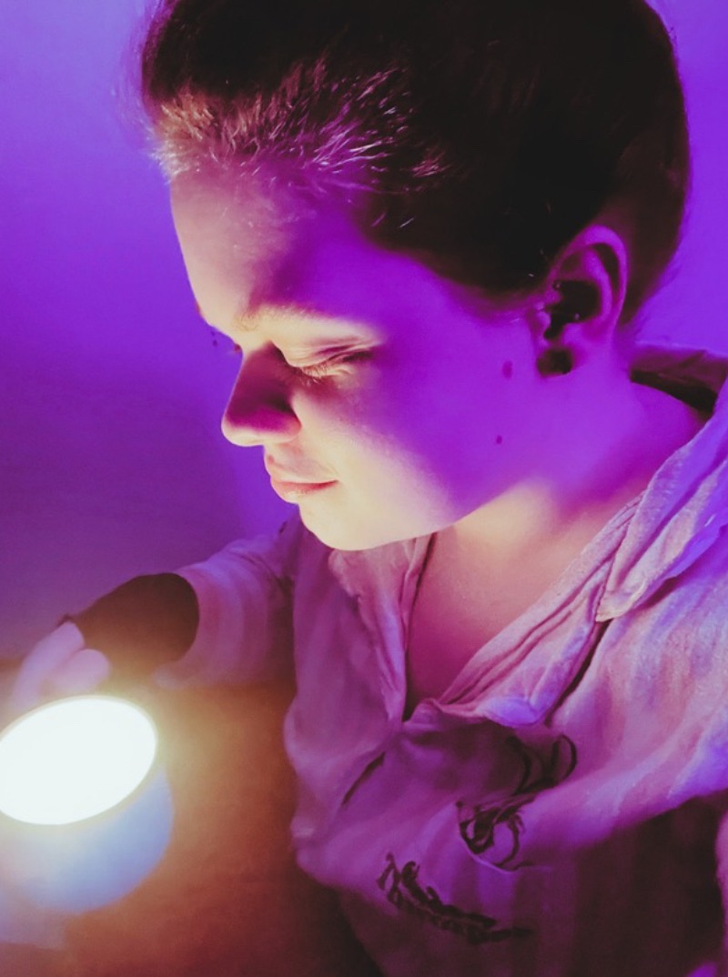 Tig holds a mug candle that they look down at with a small smile 