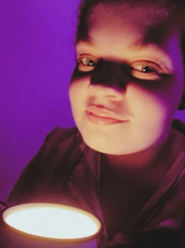 Tig holds a mug candle whilst looking at the camera with a smile 