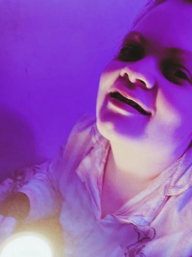 Tig holds a mug candle whilst looking up to the camera, hand leant backwards, and smiles 