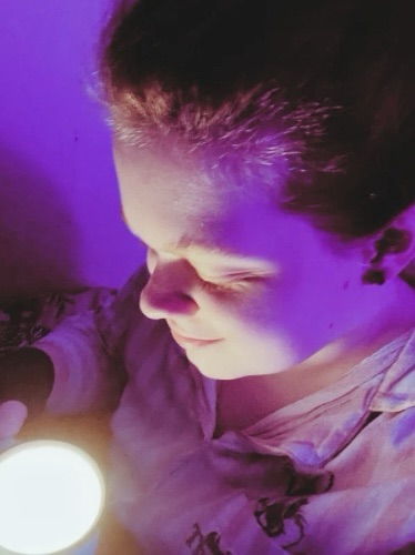 Tig holds a mug candle that they look down at with a small smile 