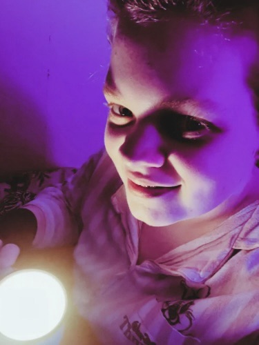 Tig holds a mug candle whilst looking up to the camera and smiles 