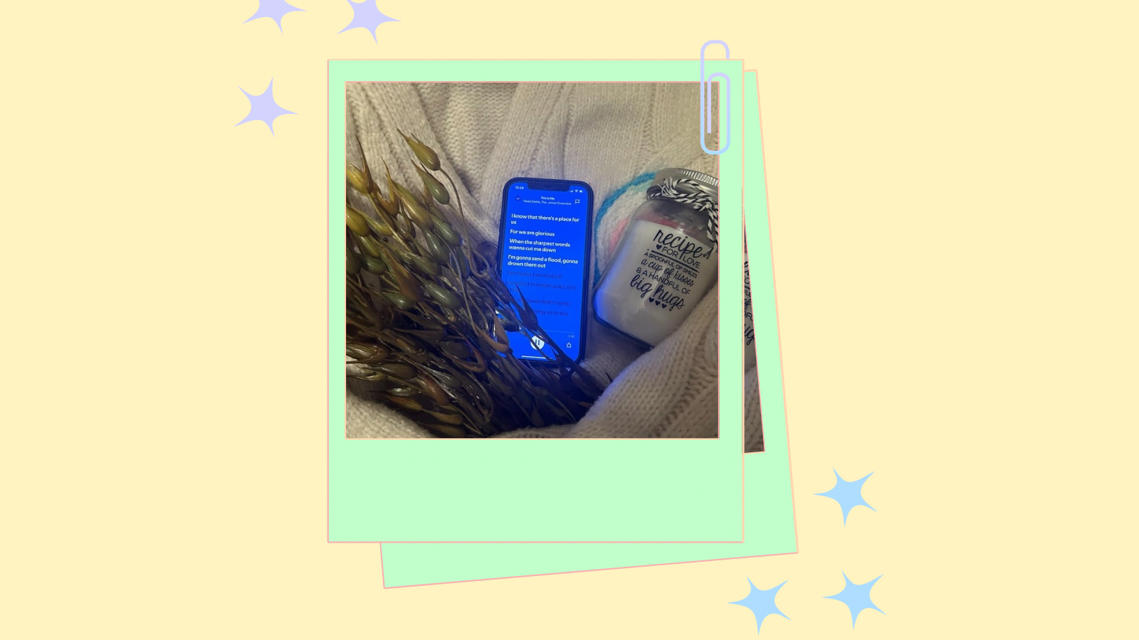 A cartoon style polaroid of an artificial seaweed plant, a phone displaying lyrics and a candle held in an empty cardigan. The background features a light orange setting with cartoon stars.
