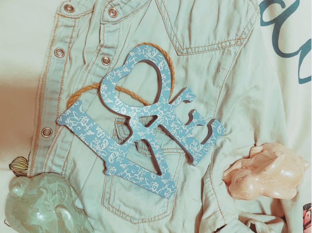 Two pastel ceramic bunnies, a milkshake style candle and a blue wooden ‘love’ sign with a white lace design lay on a denim shirt on a bed.